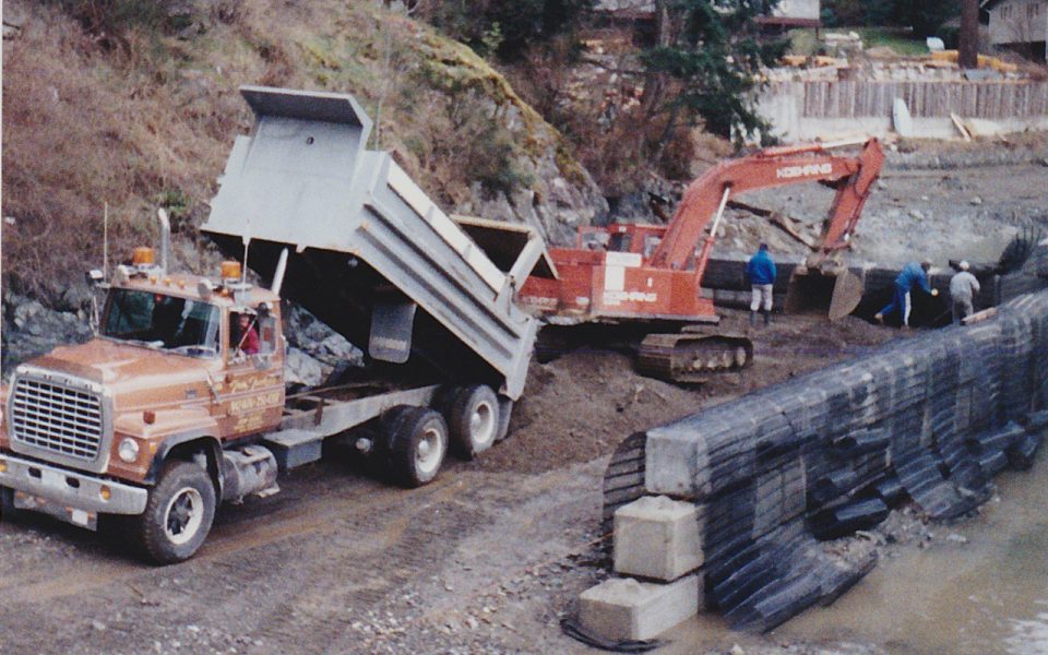 Dump truck and excavator working to move soil at a marina