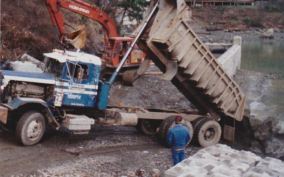 Dump truck dumping soil with an excavator in the background