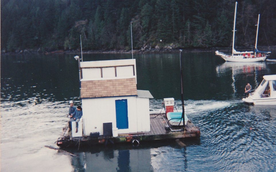 Small building and gas pump being towed into a marina