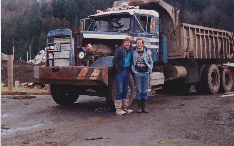 Two men standing in front of a large dump truck
