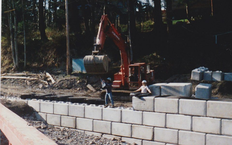 Two men and an excavator putting concrete blocks in a wall