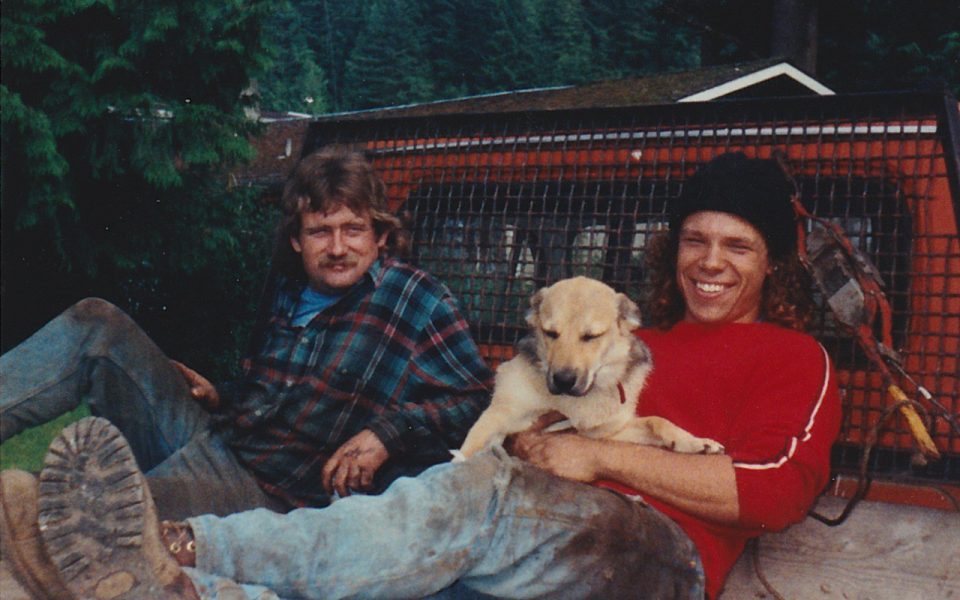 Two men and a dog sitting in the back of a truck