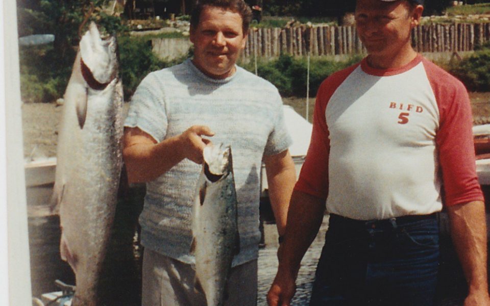 Two men one holding up a fish with another fish beside them