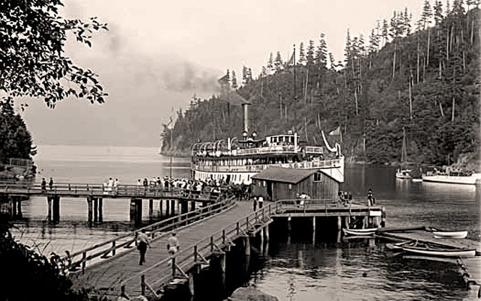 Black and white photo of old steamship about to dock on pier with two walkways