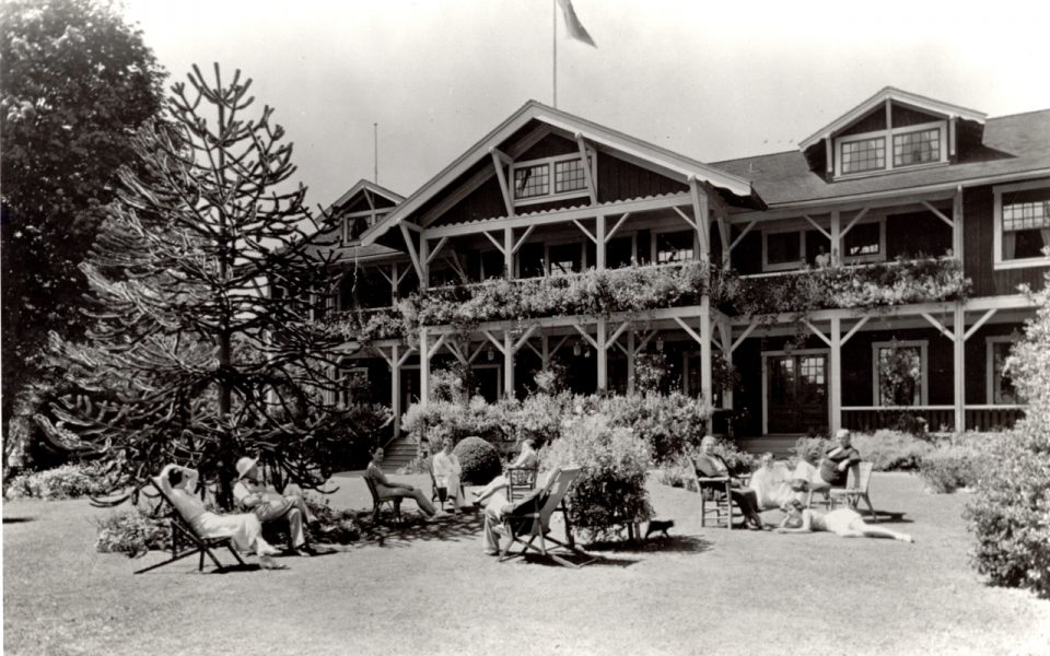 Black and white picture of old hotel with people sitting on lawn