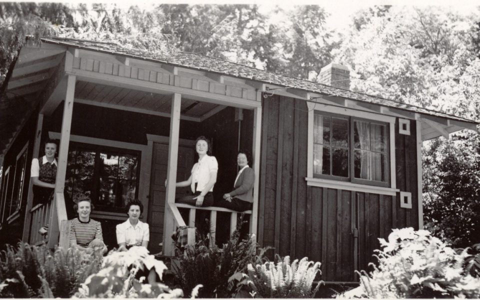 Black and white photo of cottage with people standing on the deck